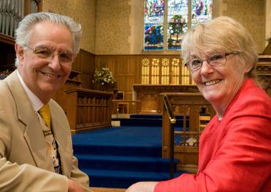 Peter and Vivien sitting in the pews inside St Luke's Church, smiling at the camera